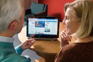 Ein älteres Paar am Computer, auf dem Bildschirm sieht man die Facebook-Seite des VdK Deutschland