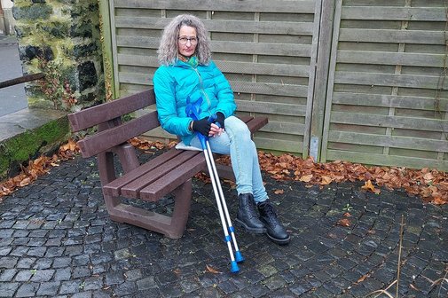 Tanja Gro&szlig; sitzt im Freien auf einer Bank, neben sich ihre Kr&uuml;cken.