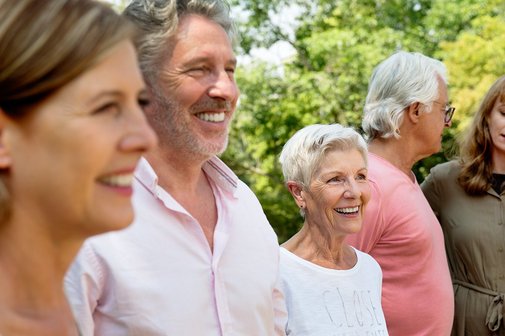 Mehrere Männer und Frauen sind gut gelaunt, lachen. Sie sind draußen im Grünen. 
