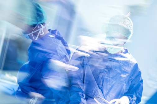 Verschwommene Aufnahme zweier männlicher Chirurgen während einer Operation, sie tragen blaue OP-Kleidung