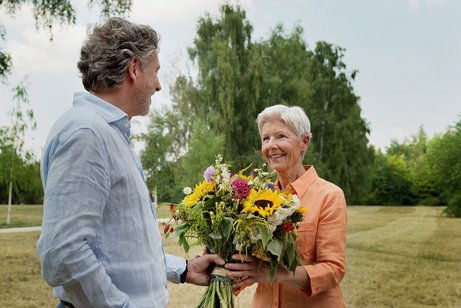 Blumenstrauß als Dankeschön Ein Mann überreicht einer älteren Frau einen großen bunten Blumenstrauß.