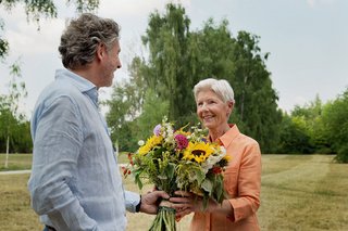 Ein Mann überreicht einer älteren Frau einen großen bunten Blumenstrauß.