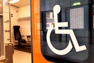 Blick in einen Bahnwaggon einer Regionalbahn mit einem Sitzplatz f&uuml;r Fahrg&auml;ste im Rollstuhl. Au&szlig;en an der Fensterscheibe ist ein gro&szlig;es Rollstuhl-Symbol.