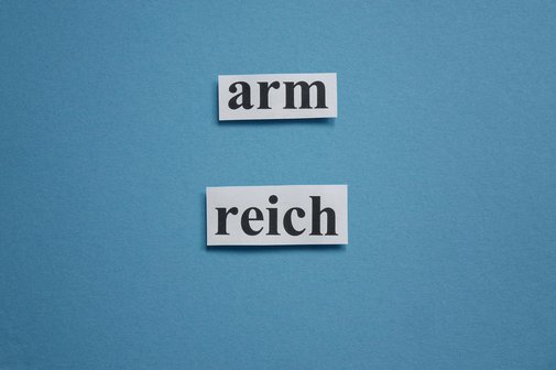 Auf blauem Grund stehen die Wörter "arm" und "reich" aus ausgeschnittenem Papier