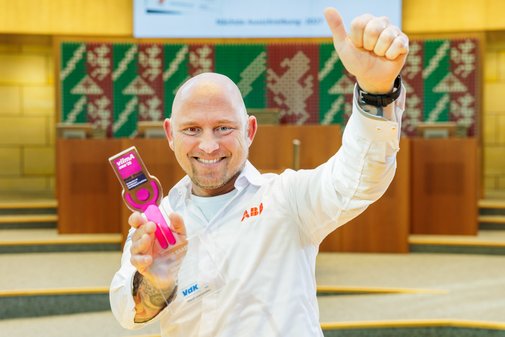 Ein Mann mit Glatze und kurzem, blonden Kinnbart und wei&szlig;em Hemd h&auml;lt l&auml;chelnd den vilmA-Preis in der Hand. Die andere Hand h&auml;lt er mit Daumen hoch in die Luft. .