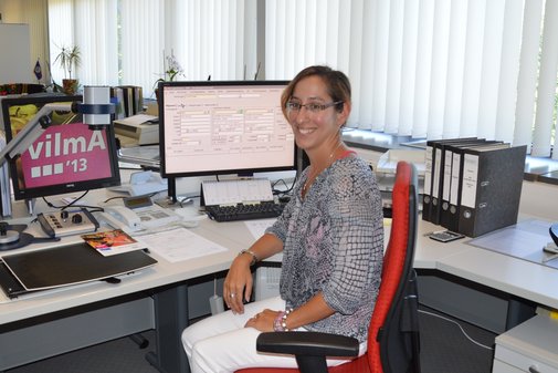 Eine vilmA-Gewinnerin sitzt an ihrem Arbeitsplatz am PC und lächelt Richtung Kamera.