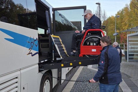 Au&szlig;en an einem Reisebus wird ein Rollstuhlfahrer mit Hebeb&uuml;hne in den Bus gehoben.
