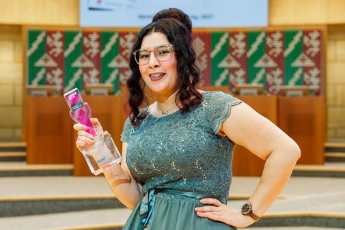 Eine Frau mit dunklen, hochgesteckten Locken in pastellgr&uuml;nem Abendkleid h&auml;lt l&auml;chelnd den vilmA-Preis in der Hand, die andere Hand an die H&uuml;fte aufgest&uuml;tzt.