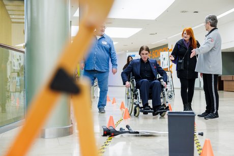 Ein Mensch im Rollstuhl versucht einen mit Pylonen abgesteckten Parcours entlang zu fahren.