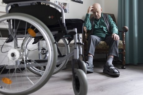 Ein alter Mann mit Rollstuhl sitzt einsam in einer Zimmerecke