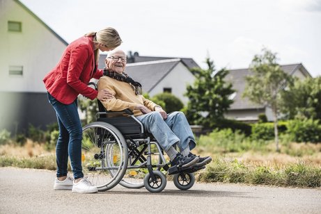 Eine junge Frau geht mit einem älteren Rollstuhlfahrer spazieren