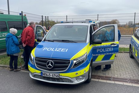 Eine Gruppe Menschen schaut rechts und links in ein Polizei-Einsatzfahrzeug.