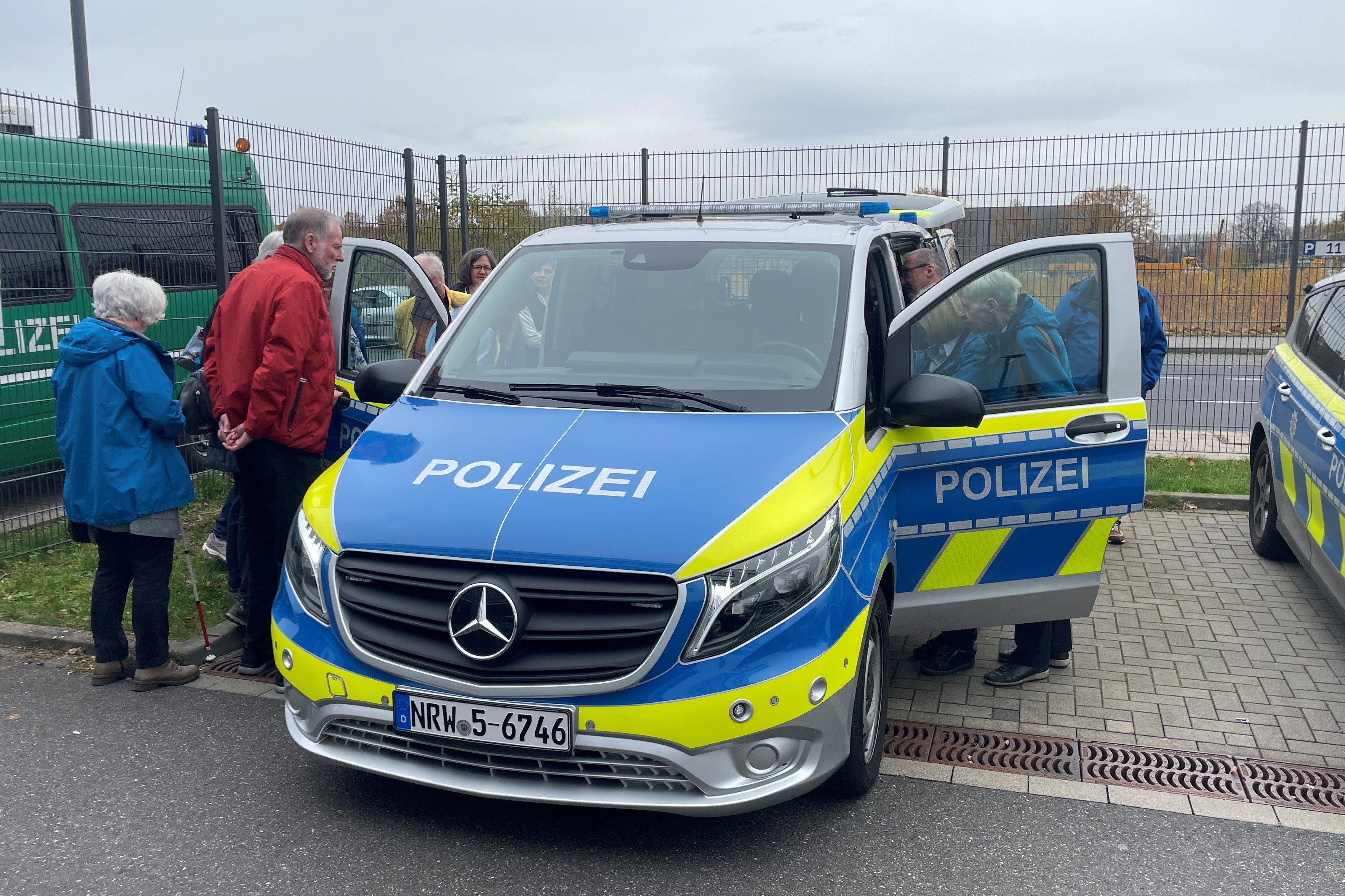 Eine Gruppe Menschen schaut rechts und links in ein Polizei-Einsatzfahrzeug.
