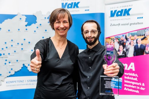 vilmA-Preisträger und Laudatorin Arm in Arm vor einer VdK-Pressewand mit vilmA-Logo.