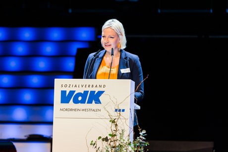 Bürgermeisterin Clara Gerlach steht am blumengeschmückten VdK-Rednerpult auf der Bühne. 