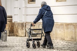 Eine alte Frau schiebt ihren Rollator über Kopfsteinpflaster