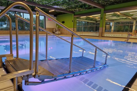 Eine flache Treppe mit Gel&auml;nder f&uuml;hrt ins beleuchtete Becken in der Schwimmhalle. 