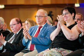 Menschen sitzen nebeneinander im Saal und applaudieren.