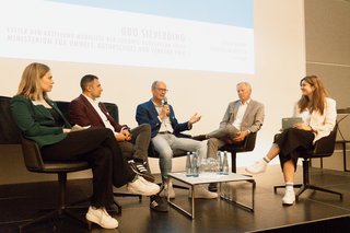 Die Teilnehmer der Podiumsdiskussion diskutieren gemeinsam auf der Bühne. 