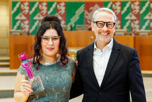Eine Frau mit Brille und undklen, hochgesteckten Locken h&auml;lt in einer Hand den vilmA-Preis. Neben ihr in Hemd und Anzug ein Mann mit Brille und grauem Kurzhaarschnitt. 