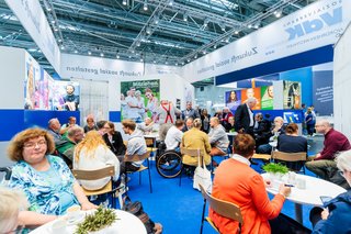 Viele Besucher sitzen an Tischen verteilt am Stand des VdK NRW.