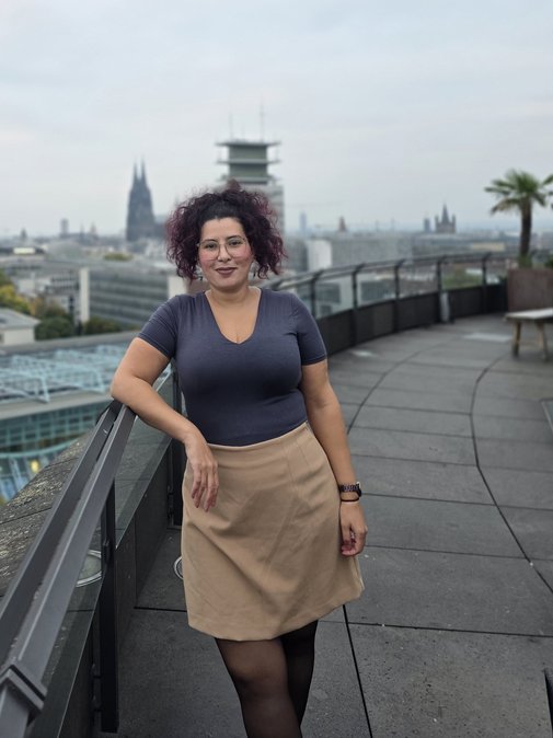Porträt von Faowzia Möwes auf einem Balkon. Im Hintergrund ein Blick auf Köln und den Dom.
