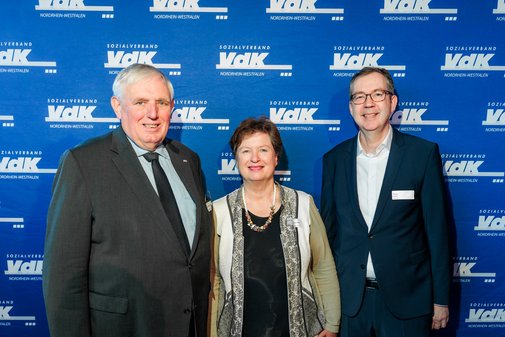 Vor einer blauen Wand mit der wei&szlig;en Aufschrift VdK schauen Minister Laumann (links), Prof. Dr. Ute Klammer (Mitte) und VdK-Vorstandssprecher Thomas Zander in die Kamera.