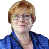 Freigestelltes Portrait einer Frau mit kurzen rotblonden Haaren und dunkelumrandeter Brille. Sie trägt eine weißgepunktete blaue Bluse und eine schmale Halskette.