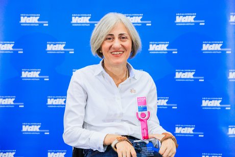 Porträt von Eleni Fischer vor blauer Wand mit weißen VdK-Logos