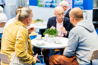 Horst Vöge sitzt mit Besuchern im Gespräch an einem Tisch.