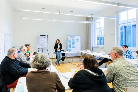 Präsenzveranstaltung Dozentin steht vor einer Gruppe von Ehrenamtlichen.