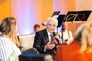 Robert Walter sitzt in der Podiumsdiskussionsrunde und spricht in ein Mikrofon