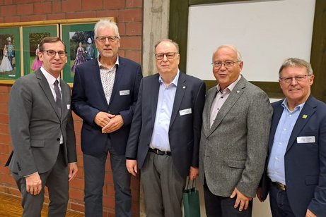 Fünf ältere Herren in Anzügen stehen vor der Fassade eines Fachwerkhauses.
