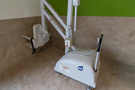 Ein Lifter steht in der Ecke eines hellgefliesten Raumes mit gr&uuml;n-wei&szlig;en W&auml;nden.