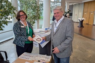 Eine Frau steht an einem Infostand und überreicht einem Mann eine VdK-Broschüre.