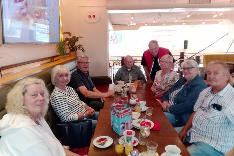 Eine Gruppe Männer und Frauen sitzt gemeinsam in einem Café an einem Tisch.