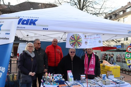 F&uuml;nf Menschen stehen an einem Tisch unter einem wei&szlig;en Pavillon mit VdK-Logo