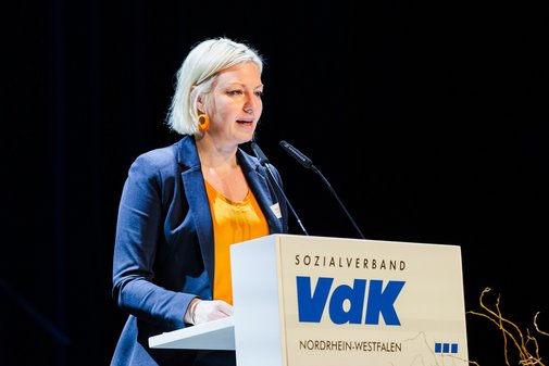 Die Düsseldorfer Bürgermeisterin Clara Gerlach, eine Frau mit blonden kinnlangen Haaren, steht an einem Redepult mit VdK-Logo und spricht ins Mikrofon.