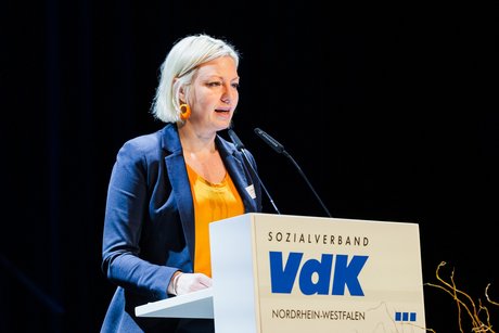 Die Düsseldorfer Bürgermeisterin Clara Gerlach, eine Frau mit blonden kinnlangen Haaren, steht an einem Redepult mit VdK-Logo und spricht ins Mikrofon.