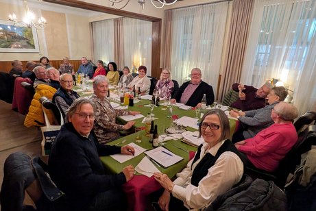 Eine Gruppe Menschen sitzt in einem Saal an einem langen Tisch.