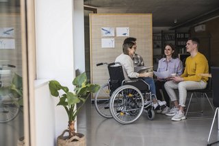 Eine Frau im Rollstuhl sitzt mit ihren Kollegen in einem Meeting