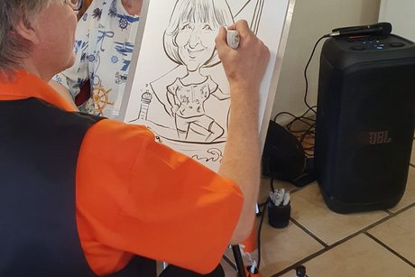 Eine Zeichnerin sitzt gegenüber einer Frau und zeichnet sie als Karikatur auf ein Blatt Papier.