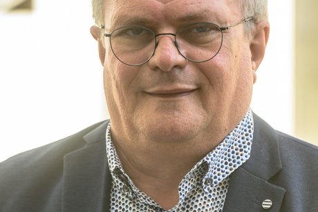 Älterer Mann mit grauen, kurzen Haaren und runder Brille in Hemd und Sakko