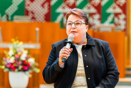 Eine Frau mit Brille und Kurzhaarschnitt spricht in ein Mikrofon. Im Hintergrund das mit Blumen geschmückte Rednerpult im Plenarsaal des Landtags NRW.