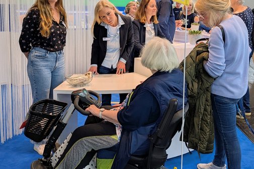 Besucher im Rollstuhl und stehend am Messestand des VdK NRW. 