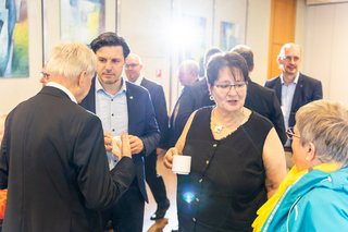 Ein Mann und eine Frau stehen mit Kaffeetassen in der Hand nebeneinander im Foyer der Stadthalle und unterhalten sich mit zwei weiteren Gästen.