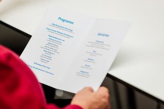 Eine Hand hält einen Zettel mit Programm und Getränke-Karte.