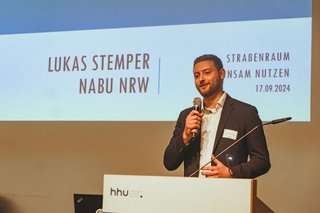 Lukas Stemper, stellvertretender Landesvorsitzender des NABU NRW, steht am Rednerpult und richtet Grußworte ans Publikum. 