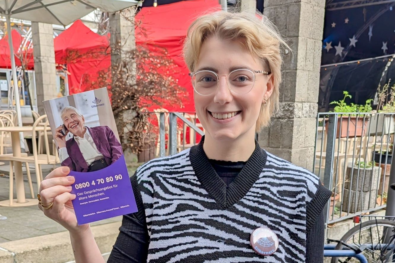 Sophia Nagelschmidt hält einen Flyer für das Projekt „Silbernetz gegen Einsamkeit im Alter in NRW" in die Kamera..