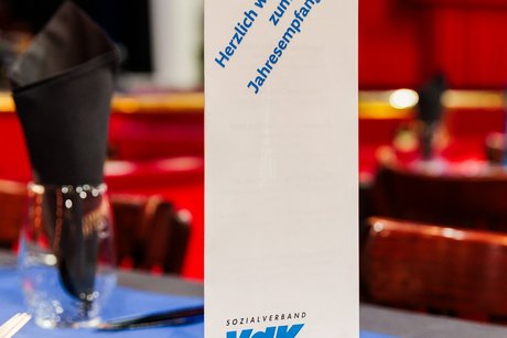 Eine weiße Klappkarte mit der Aufschrift herzlich Willkommen zum Jahresempfang und Logo des VdK NRW steht hochkant auf einem Tisch.